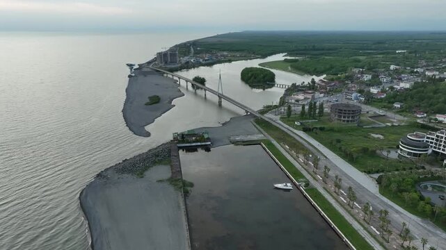 Aerial view of Anaklia resort in Georgia featuring the futuristic observation tower, pedestrian bridge over Enguri river, sandy beach, and Black Sea coastline on a sunny day.