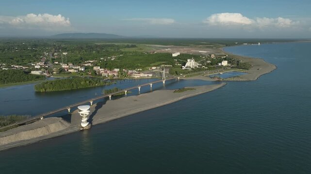 Aerial view of Anaklia resort in Georgia featuring the futuristic observation tower, pedestrian bridge over Enguri river, sandy beach, and Black Sea coastline on a sunny day.