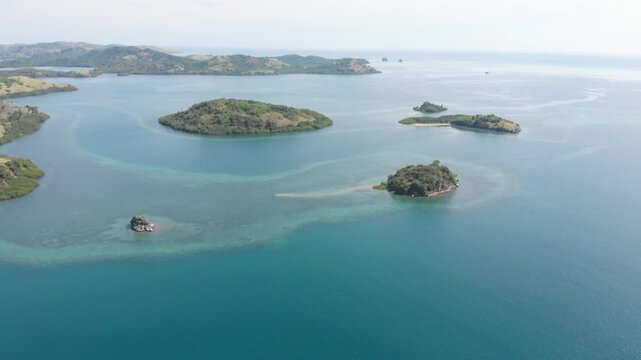 Panoramic aerial view of the 17 Islands Marine Park near Riung, Flores, Indonesia, featuring turquoise coral reefs, tropical islets, and deep blue ocean under a bright sky