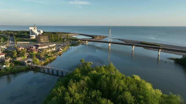 Aerial view of Anaklia resort in Georgia featuring the futuristic observation tower, pedestrian bridge over Enguri river, sandy beach, and Black Sea coastline on a sunny day.