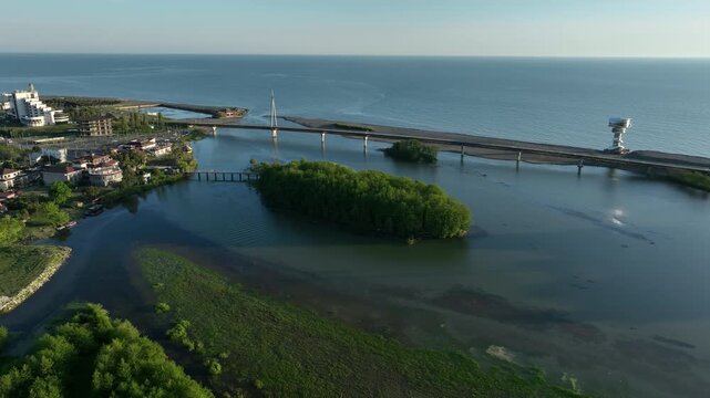 Aerial view of Anaklia resort in Georgia featuring the futuristic observation tower, pedestrian bridge over Enguri river, sandy beach, and Black Sea coastline on a sunny day.
