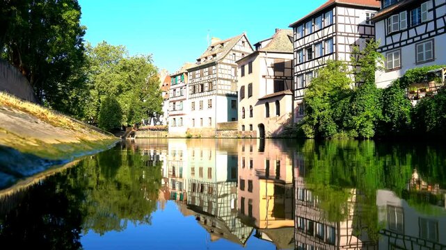 Strasbourg, France. Petite France quarter, historic half-timbered houses with steep roofs and exposed timber beams reflected in the calm Ill River under clear summer sky