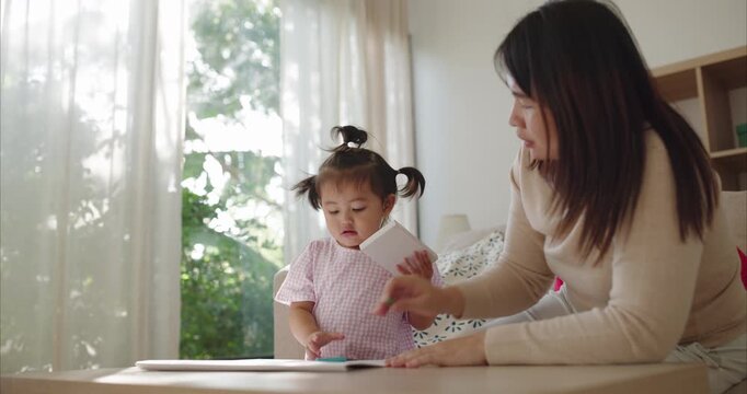 Asian Mother and Toddler Girl with Pigtails Drawing at Table; Happy Family Bonding, Learning Activity and Child Development in Cozy Bright Home Living Room