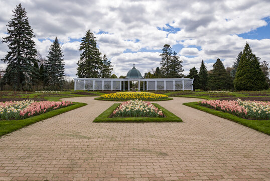 Colorful various flowers against the background of a wooden openwork gazebo - Niagara Falls Botanical Garden in spring - flowerbed flowers in the foreground,