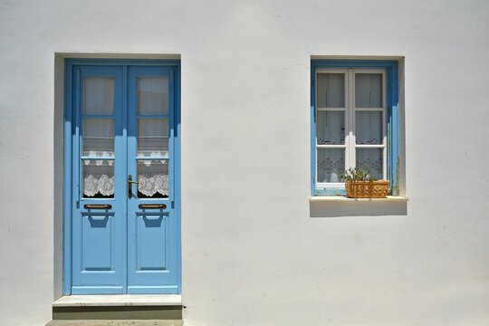 Traditional rural house facade with a whitewashed wall a light blue wooden door and window with handmade cutwork curtains in Chora, Kythira, Greece.