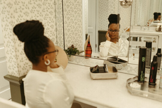 Stylish woman with braided bun looks in vanity mirror