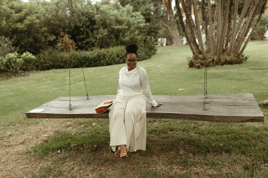 Stylish Black woman relaxing on a wooden swing outdoors