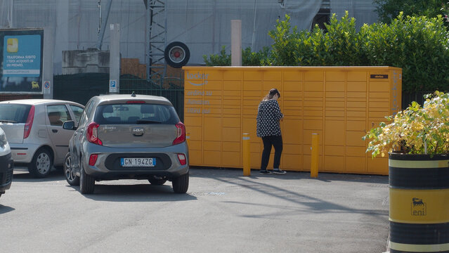 Woman collecting package from an Amazon Locker at an Eni gas station in Italy, reflecting e commerce and retail trends