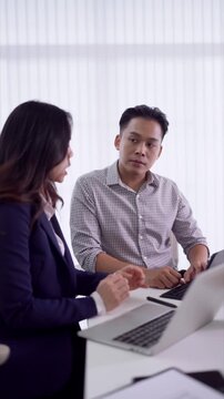 young Asian business professionals discuss project strategy using laptop computer collaborate teamwork modern office meeting conference room communication