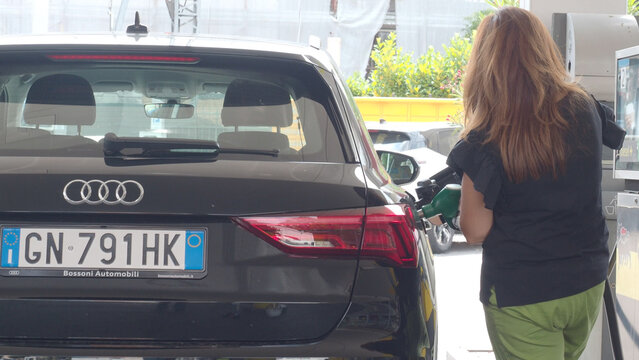 Woman refilling black Audi car at Eni fuel station in Italy, consumer spending on transportation and rising gasoline costs