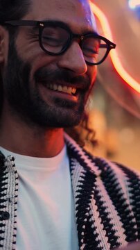 Smiling young man scrolling social media and chatting with friends on his smartphone, surrounded by vibrant neon lights. casual demeanor and lively urban setting reflect modern connectivity and joy
