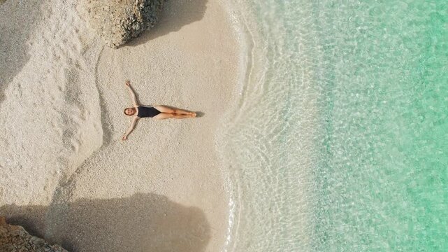 Aerial of woman relaxing on quiet beach with turquoise sea water on a calm sunny day in Kefalonia Greece