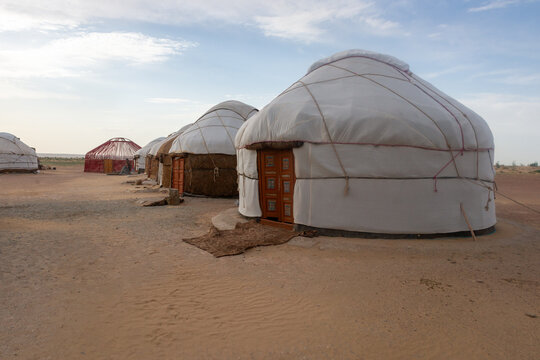 A row of traditional yurts near the Ayaz Kala fortress, Uzbekistan, with white felt coverings and wooden doors set on a flat desert plain evoking nomadic heritage, simplicity and remote rural life.
