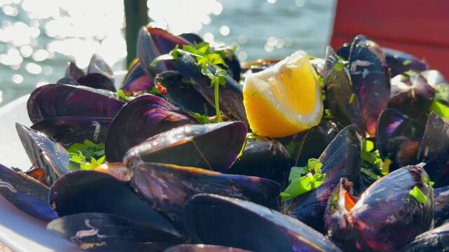 Pile of steamed dark blue mussel shell garnished with fresh lemon wedge and parsley herb served at sunny seaside restaurant, mediterranean seafood dish
