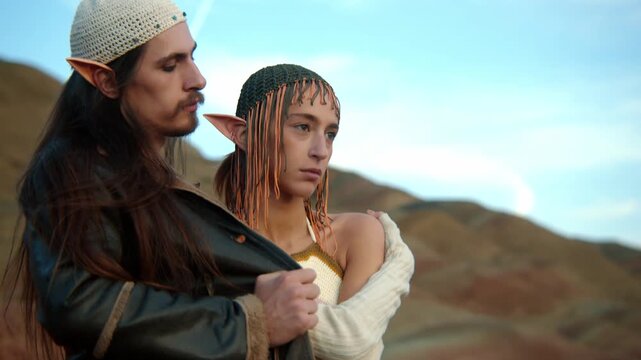 Stylish fantasy couple with elf ears posing together in a desert landscape. Cinematic lighting, flowing outfits, and surreal atmosphere create an epic fantasy-inspired fashion scene.