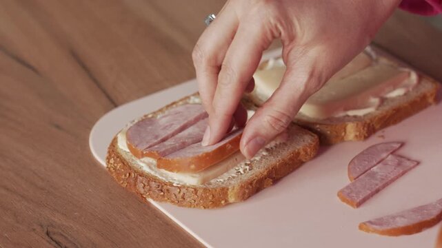 Creating a sandwich with the addition of ham. The hand places the sliced ham on the sandwich.