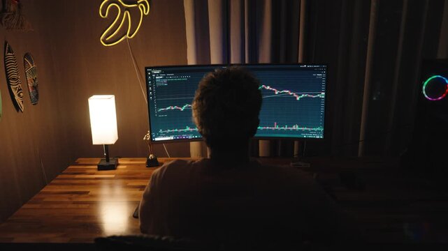 Professional trader or investor working at multiple monitors with stock market charts, financial data, and trading graphs.