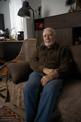 Fototapeta premium Older man sits on a couch in a cozy living room with simple decor and natural light during the afternoon