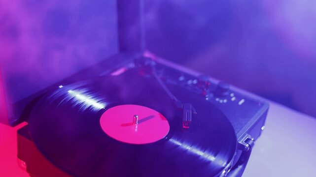 Close-up of a spinning vinyl record on a turntable with pink and blue lighting