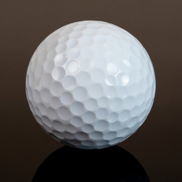 A close-up shot of a pristine white golf ball with its characteristic dimpled surface, resting on a reflective dark background, embodying the spirit of the game and precision