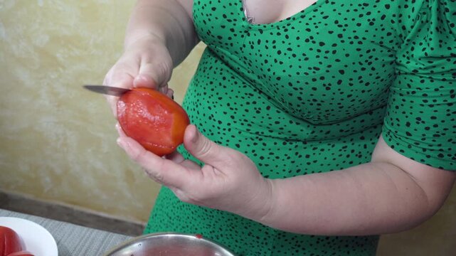 A woman peels a ripe red tomato with a kitchen knife, Close up of hands peeling a fresh tomato in the kitchen