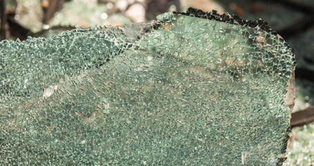 Car glass cracked and damaged car windshield was held in place by a sheet of car window film, standing upright on the ground. © saksuvan