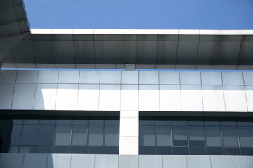 Obraz premium Low angle view of a modern office building exterior with silver metallic cladding and a flat roof structure against a clear blue sky portraying contemporary architecture and corporate real estate