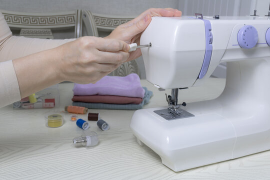 Female hands repairing a white household sewing machine with a screwdriver in a home workshop, DIY repair and adjustment concept, hobby.