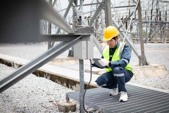 Utility engineer inspecting a substation junction box and support structure during field maintenance, documenting safety checks for electrical infrastructure reliability