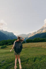 Fototapeta premium Hiking woman with backpack in a sunlit meadow, mountains in the background, exploring nature and outdoors in a vibrant travel moment