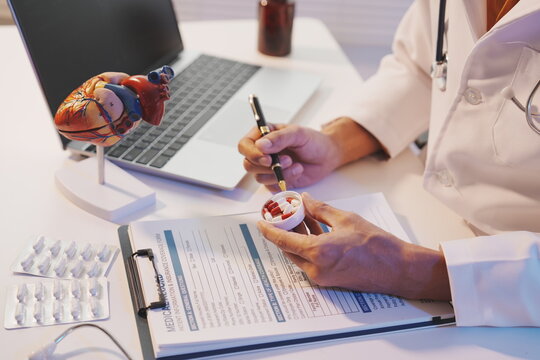 A doctor is shown writing on a medical form while holding a small cap filled with white and red capsules, illustrating the prescription process. 