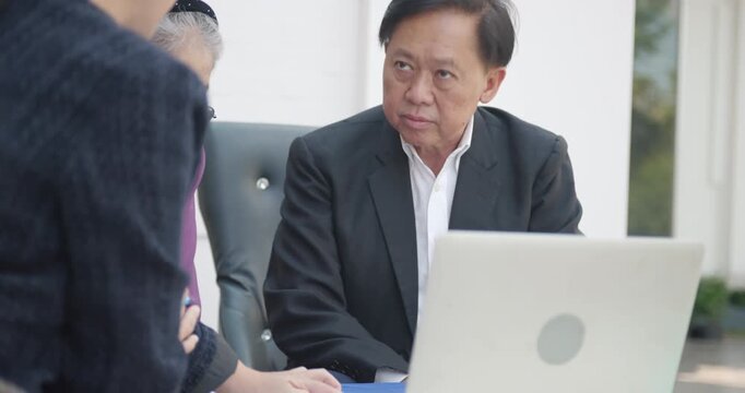 Senior Asian couple listening to a financial advisor or real estate agent presenting on a laptop.