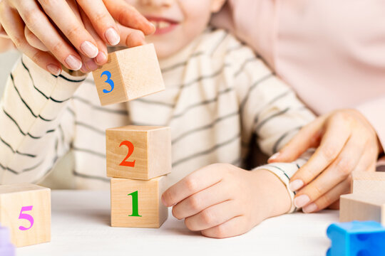Mother or teacher helping child with math using wooden numbers blocks. Concept of early childhood education, mental development and homework support at home.