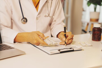 A focused shot of a doctor’s hand writing on a clipboard with a chart. A miniature brain model stands on the desk, near a laptop showing a patient outline graphic.  © Yanisa