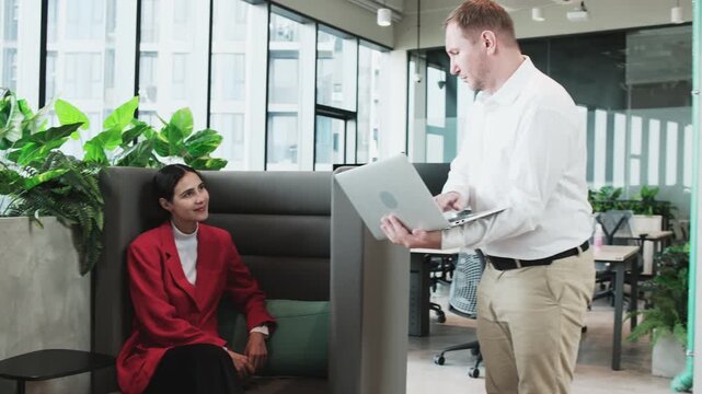 Two business coworkers, female Latin CEO manager and White employee, seriously discuss and consult a financial job project on laptop at modern workplace near window, collaboration problem solution.