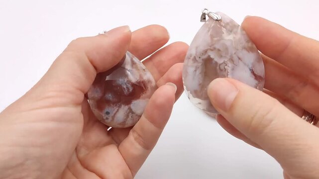 Three polished cherry blossom agate gemstone pendants in a smooth teardrop shape are displayed in an open hand, showcasing unique translucent pink and white floral patterns