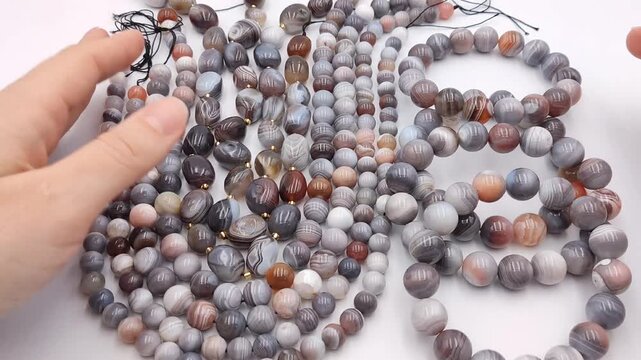 Polished grey and brown banded agate stone beads are arranged in loose strands and hand held circles, showcasing natural circular mineral patterns for custom wholesale artisan jewelry design