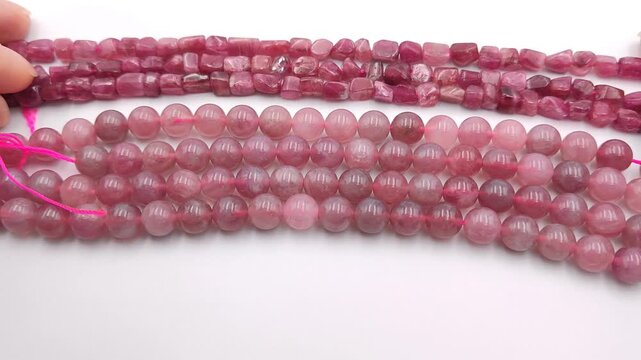Natural pink tourmaline strands featuring polished round beads and irregular smooth pebble shapes are aligned on a clean white background for artisan crystal jewelry creation supplies