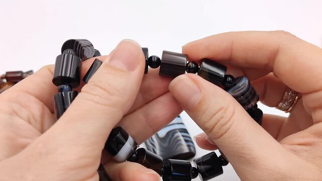 Polished black agate cylinder beads with natural white stripes are carefully held and inspected, showcasing unique banded patterns for custom artisan jewelry making components