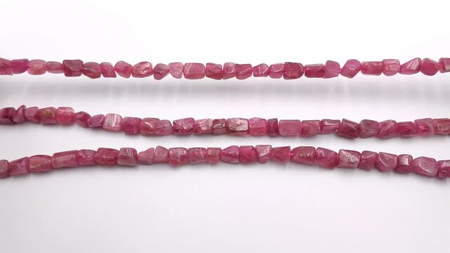 Three strands of natural pink tourmaline gemstone nugget beads on a plain white background wrapping them around a wrist to show texture and color quality