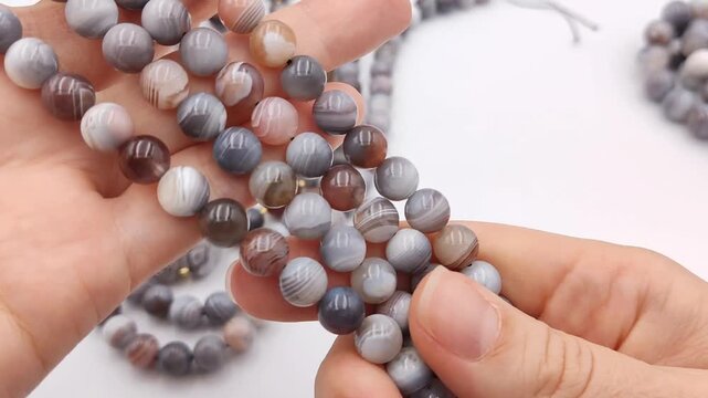 Smooth grey and white striped agate beads are gathered in a hand, showcasing unique circular mineral patterns perfect for crafting handmade artisan jewelry