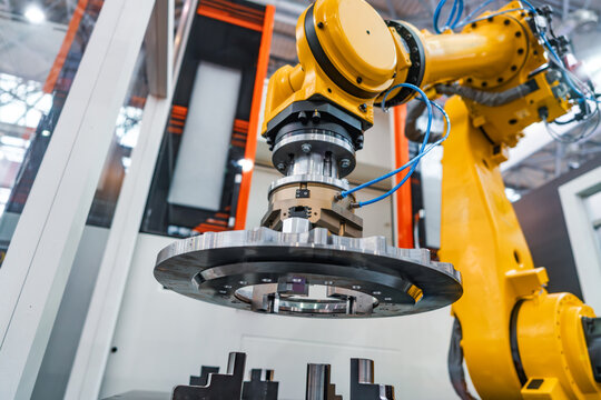 Industrial robotic arm holding metal gear component in automated factory cell.