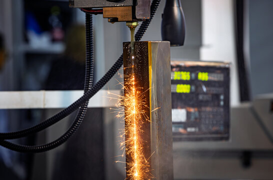Wire EDM cutting of metal workpiece with sparks in industrial machine.