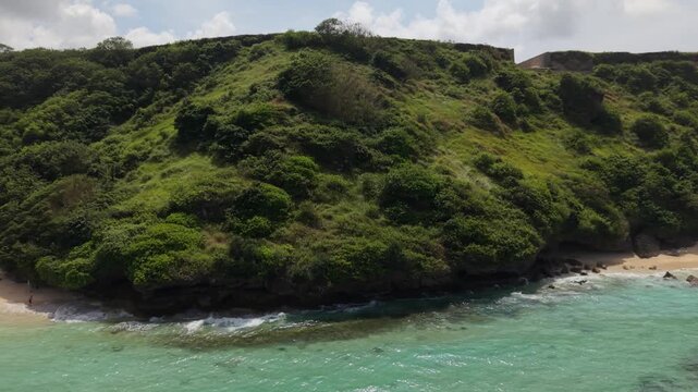 Aerial View of Gunung Payung Beach with Turquoise Ocean Waves and Lush Green Cliff in Bali