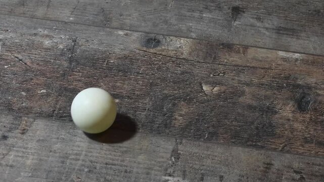 Ping pong ball rolls on wooden floor after bouncing from a height