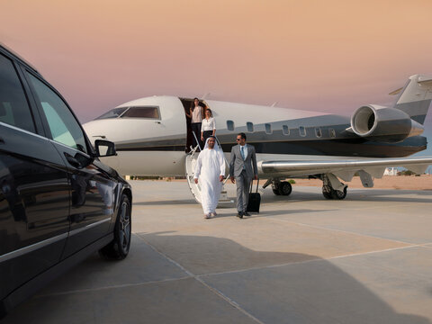 Middle Eastern business team exiting private jet on runway beside luxury car at sunset