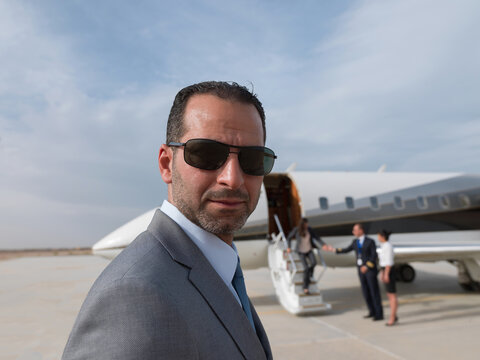 Middle Eastern business team arriving at private jet on airport tarmac with security and staff
