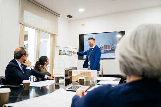Team of architects and executives meeting, manager presenting new housing project plans and building models to colleagues