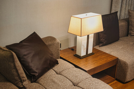 A moody, modern living room featuring a marble-based table lamp that casts a warm glow over a grey tufted sofa and dark accent pillows.