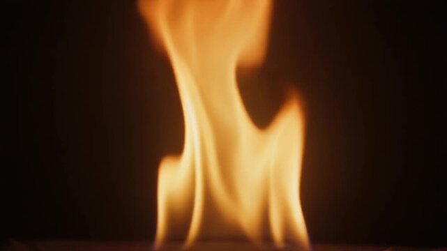 Bright orange and yellow flame burning continuously against a solid black background. Close-up static video footage of isolated fire element for visual effects compositing.